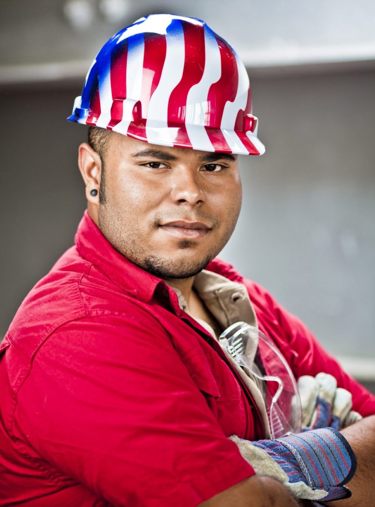 A construction worker wearing a red shirt and a patriotic striped hard hat.